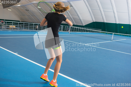 Image of The young girl in a closed tennis court with ball