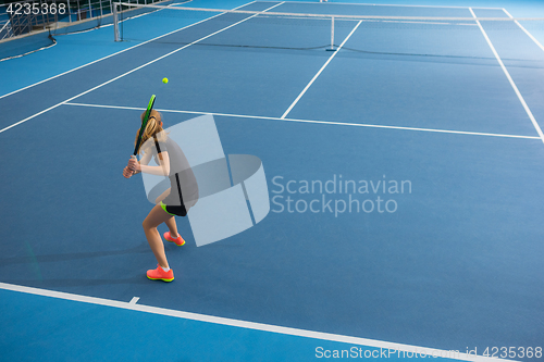 Image of The young girl in a closed tennis court with ball