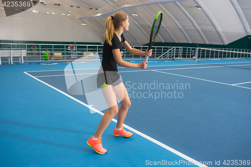 Image of The young girl in a closed tennis court with ball