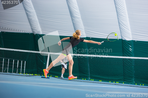 Image of The young girl in a closed tennis court with ball