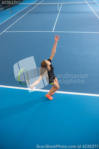 Image of The young girl in a closed tennis court with ball