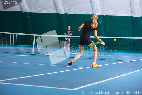 Image of The young girl in a closed tennis court with ball