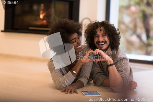 Image of multiethnic couple showing a heart with their hands on the floor