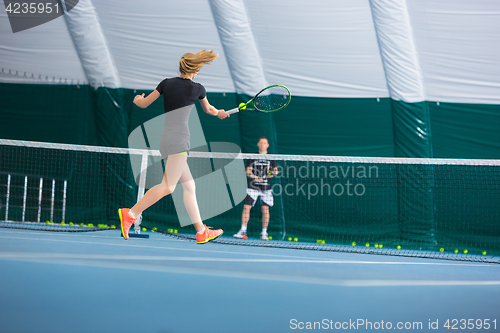 Image of The young girl in a closed tennis court with ball