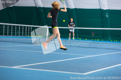 Image of The young girl in a closed tennis court with ball