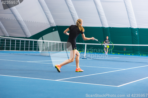 Image of The young girl in a closed tennis court with ball