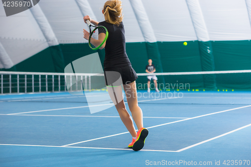 Image of The young girl in a closed tennis court with ball