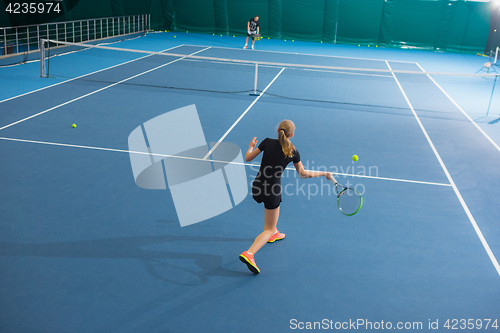 Image of The young girl in a closed tennis court with ball