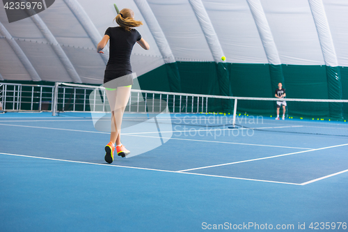 Image of The young girl in a closed tennis court with ball