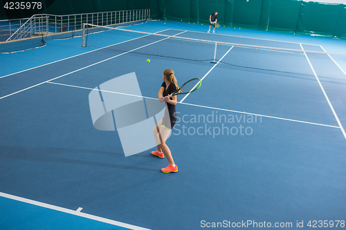 Image of The young girl in a closed tennis court with ball