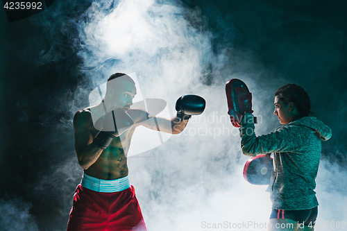 Image of Handsome Afro American boxer with bare torso is practicing punches with a partner at the fight club