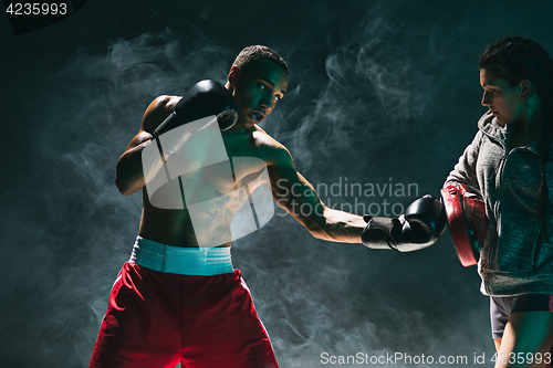 Image of Handsome Afro American boxer with bare torso is practicing punches with a partner at the fight club