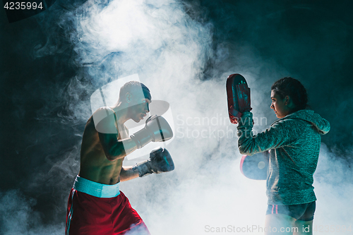 Image of Handsome Afro American boxer with bare torso is practicing punches with a partner at the fight club