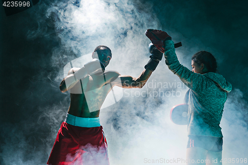 Image of Handsome Afro American boxer with bare torso is practicing punches with a partner at the fight club