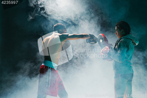 Image of Handsome Afro American boxer with bare torso is practicing punches with a partner at the fight club