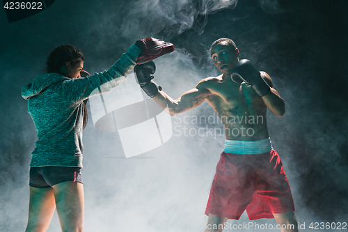 Image of Handsome Afro American boxer with bare torso is practicing punches with a partner at the fight club