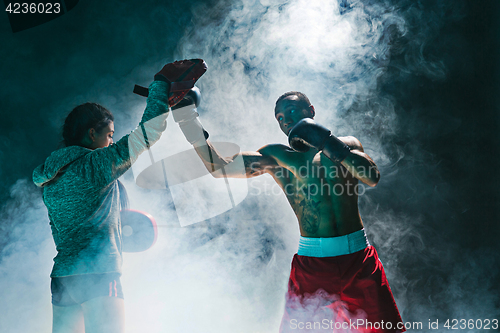 Image of Handsome Afro American boxer with bare torso is practicing punches with a partner at the fight club