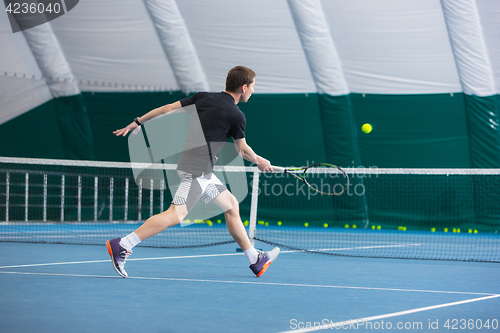 Image of The young man in a closed tennis court with ball