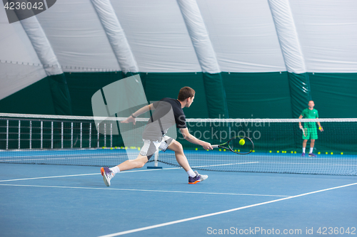 Image of The young man in a closed tennis court with ball