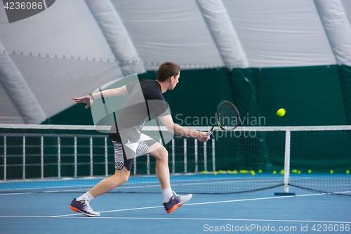 Image of The young man in a closed tennis court with ball