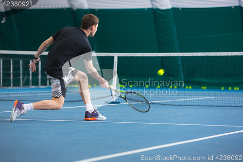 Image of The young man in a closed tennis court with ball