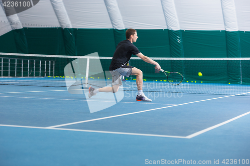 Image of The young man in a closed tennis court with ball