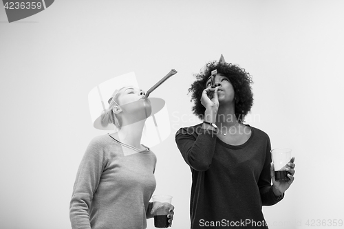 Image of smiling women in party caps blowing to whistles