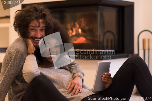 Image of multiethnic couple using tablet computer on the floor