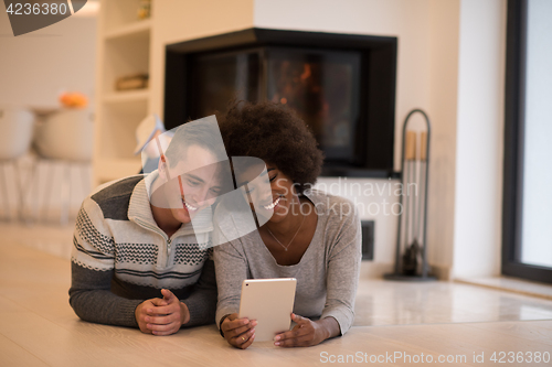 Image of multiethnic couple using tablet computer on the floor