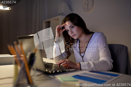 Image of businesswoman with laptop at night office