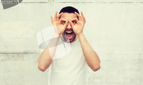 Image of man making finger glasses over gray background