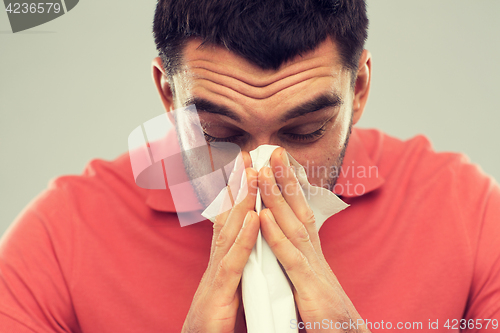 Image of sick man blowing nose to paper napkin at home