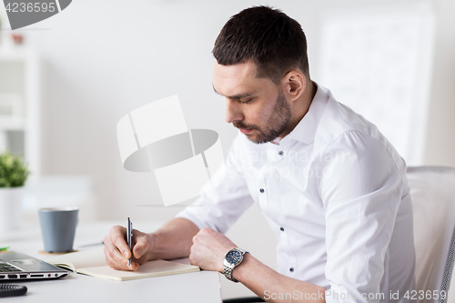 Image of businessman writing to notebook at office