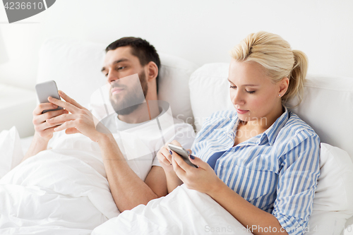 Image of couple with smartphones in bed at home