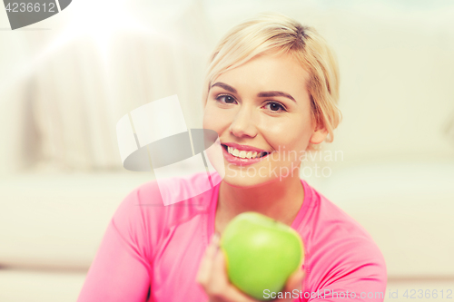 Image of happy woman eating green apple at home