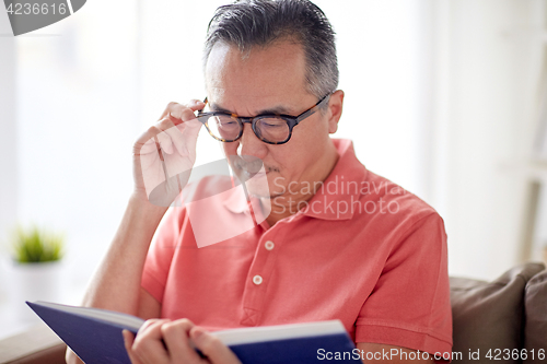 Image of man in glasses reading book at home