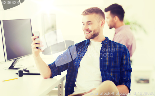 Image of happy creative man texting on cellphone at office