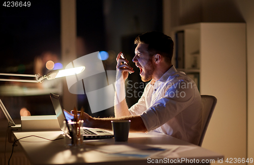 Image of angry businessman with smartphone at night office