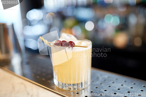 Image of glass of cocktail with cherries at bar