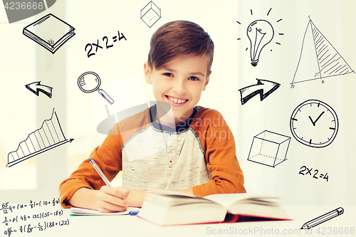 Image of smiling student boy writing to notebook at home