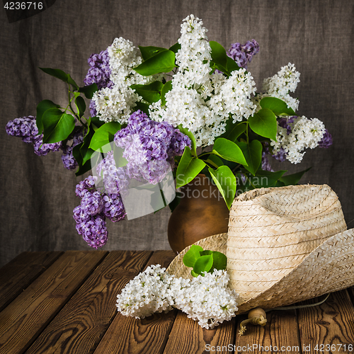 Image of Still-life with a bouquet of lilacs and a straw hat, close-up