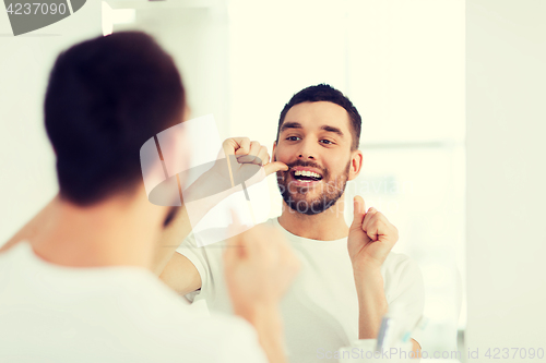 Image of man with dental floss cleaning teeth at bathroom