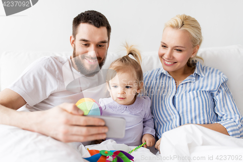 Image of happy family with smartphone in bed at home