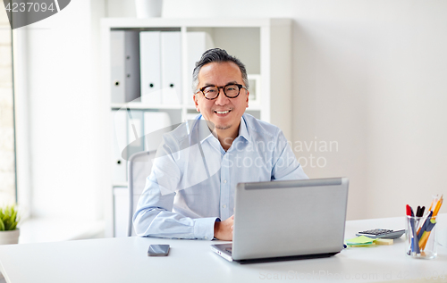Image of happy businessman in eyeglasses with laptop office