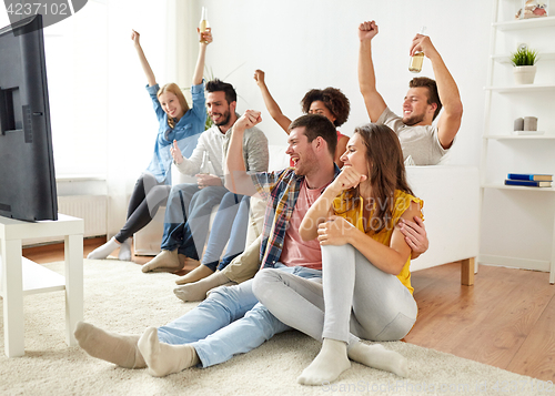 Image of happy friends with beer watching tv at home