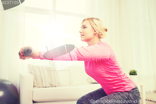 Image of smiling woman with dumbbells exercising at home