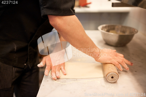 Image of chef with rolling-pin rolling dough at kitchen