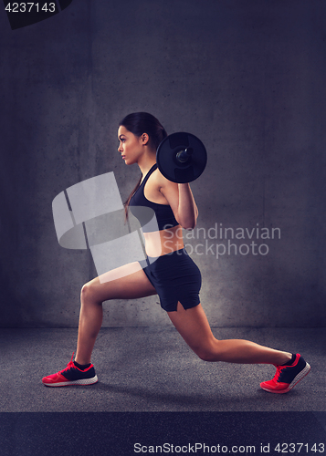 Image of young woman flexing muscles with barbell in gym