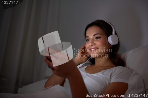 Image of woman with smartphone and headphones in bed