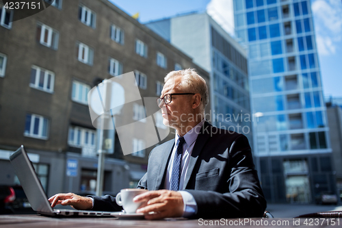 Image of senior businessman with laptop drinking coffee